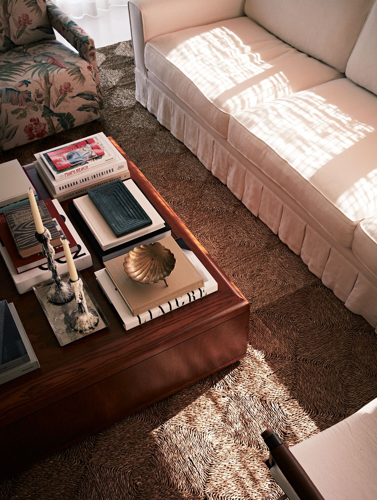 Sun across a skirted sofa and a coffee table stacked with books, by Studio DEA